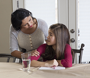 Niña haciendo la tarea y hablando con una mujer.